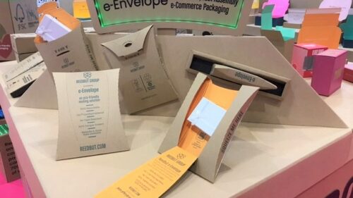 Photo of a display for the e-Envelope. The e-Envelope is a thin cardboard pack with a perforated opening flap. It is displayed closed, partly open, and fully open to reveal a small white box as its contents.